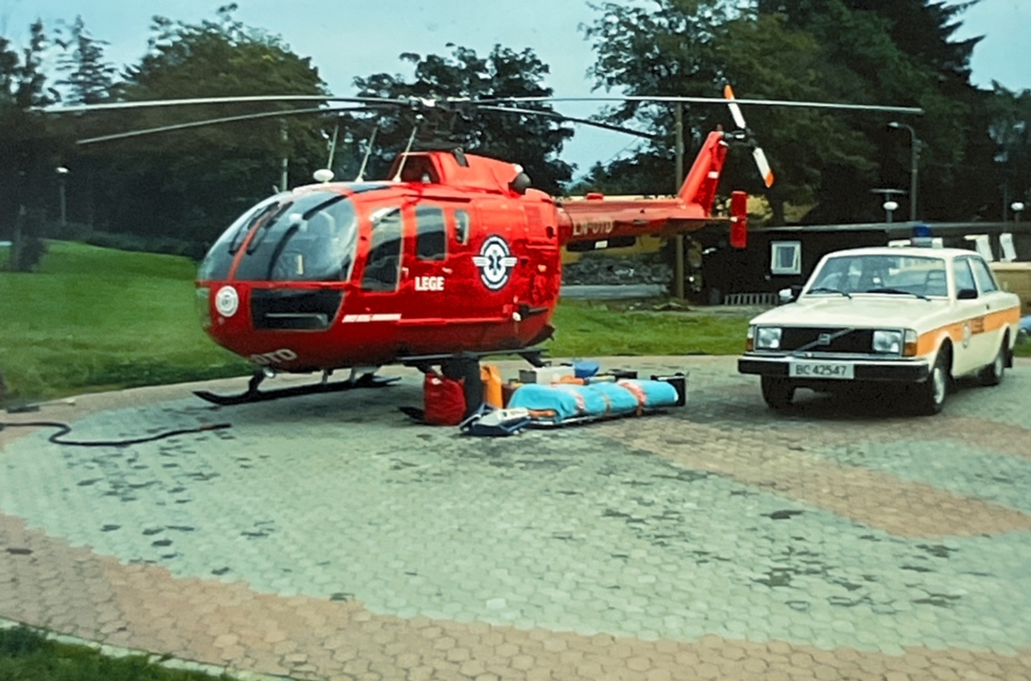 Et rødt helikopter parkert ved siden av en hvit bil