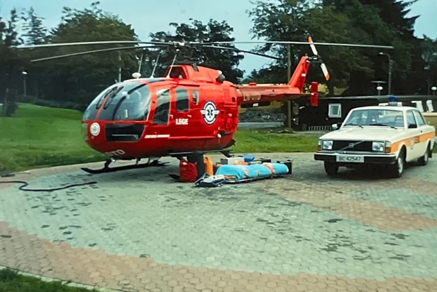 Et rødt helikopter parkert ved siden av en hvit bil