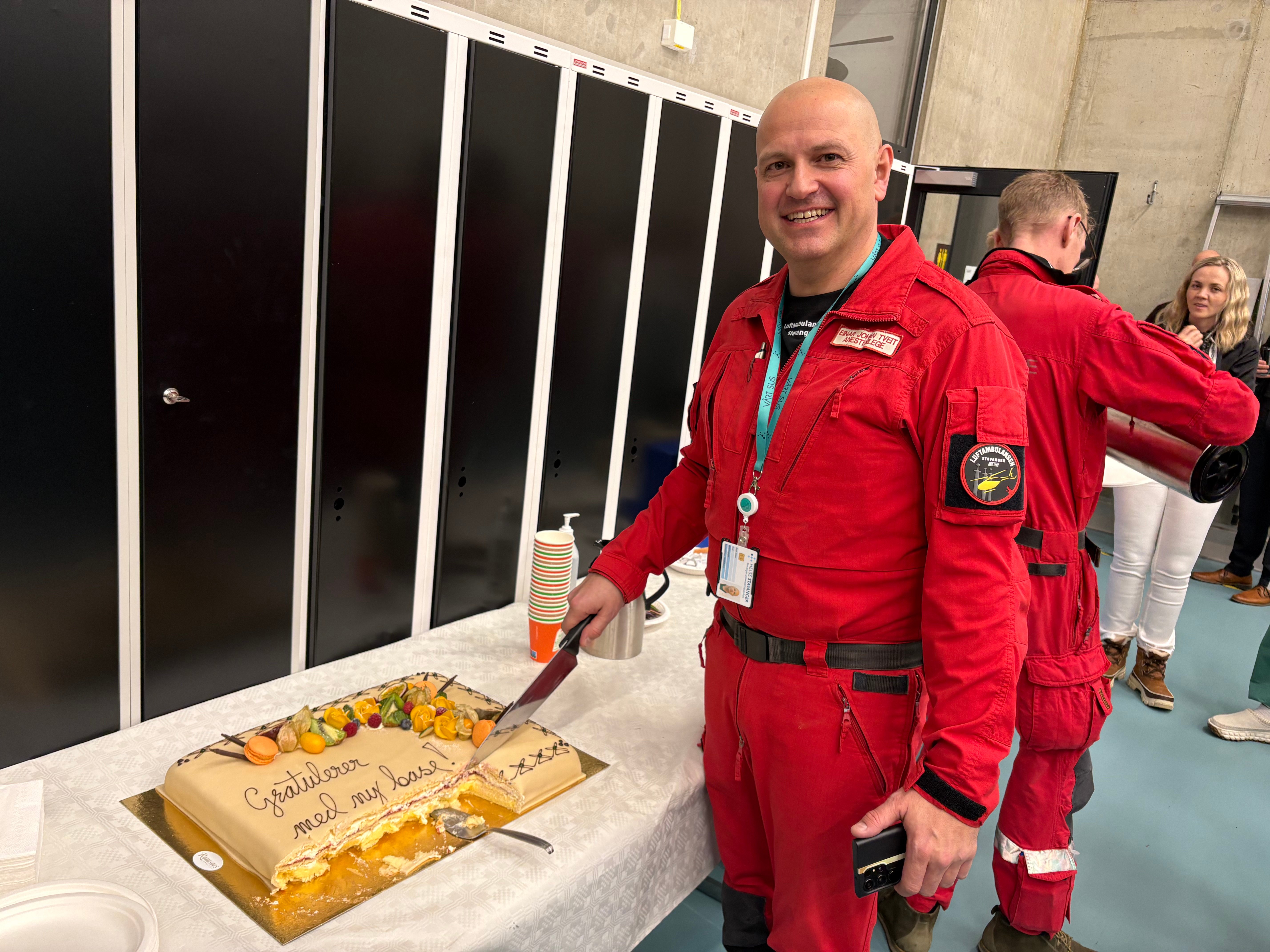 Mann i rød luftambulanseuniform foran en stor kake