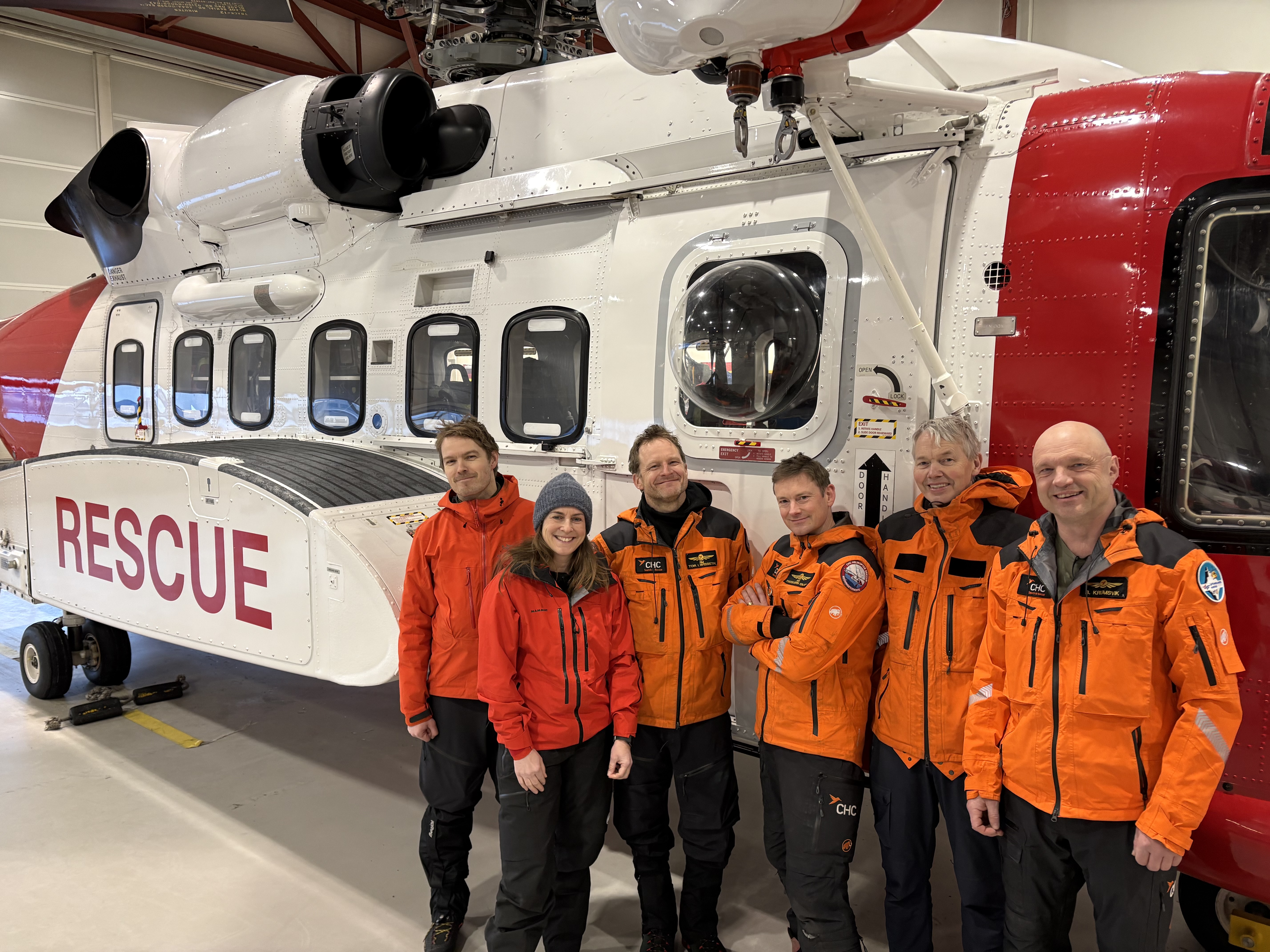 Fem menn og en kvinne i uniform foran et redningshelikopter
