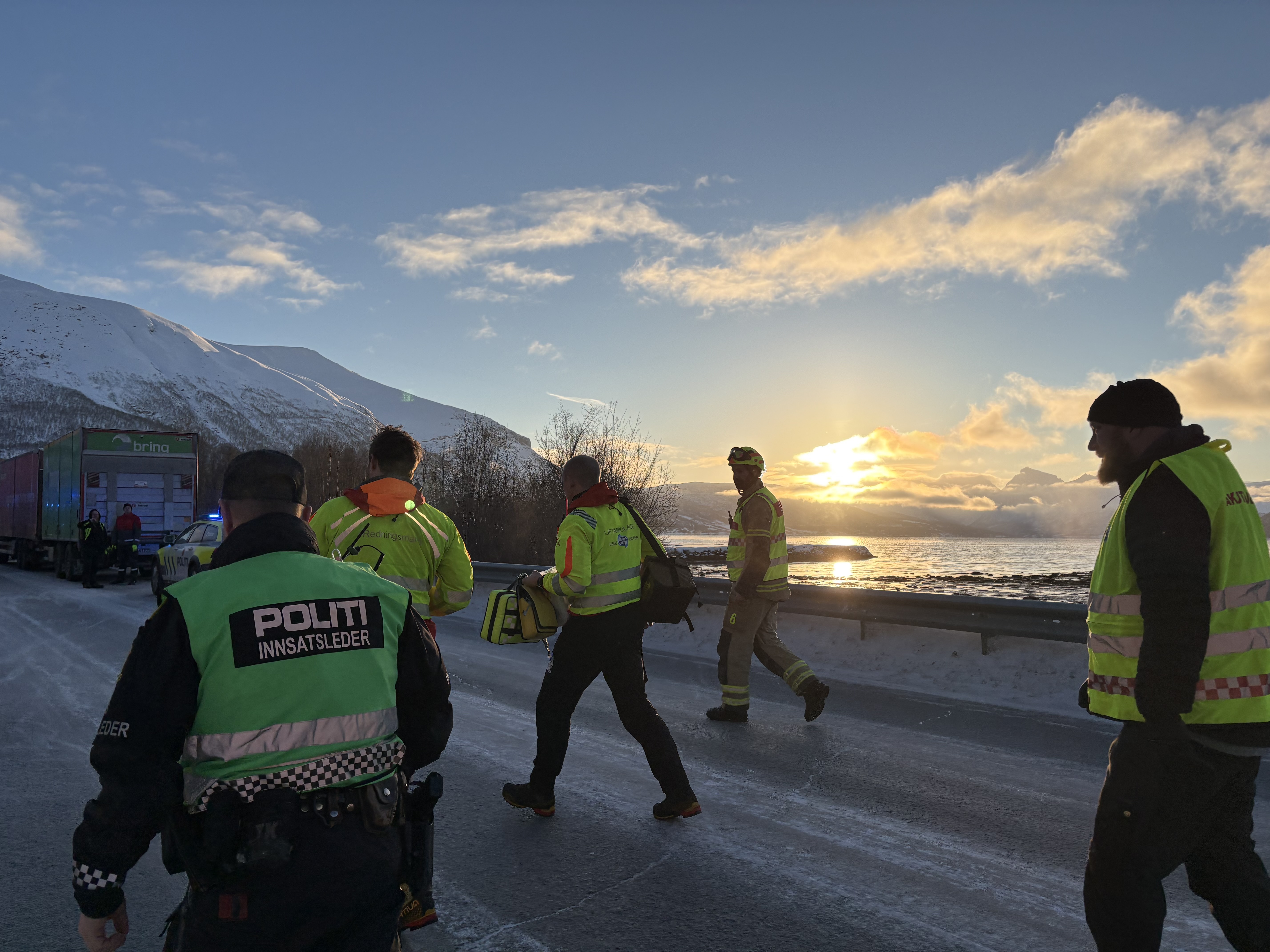 Brann, politi og ambulansepersonell som går på en vei med snø og fjell i bakgrunnen