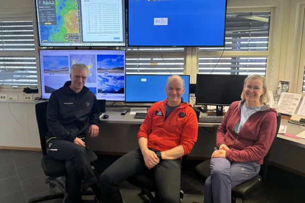 To menn og en dame foran mange skjermer