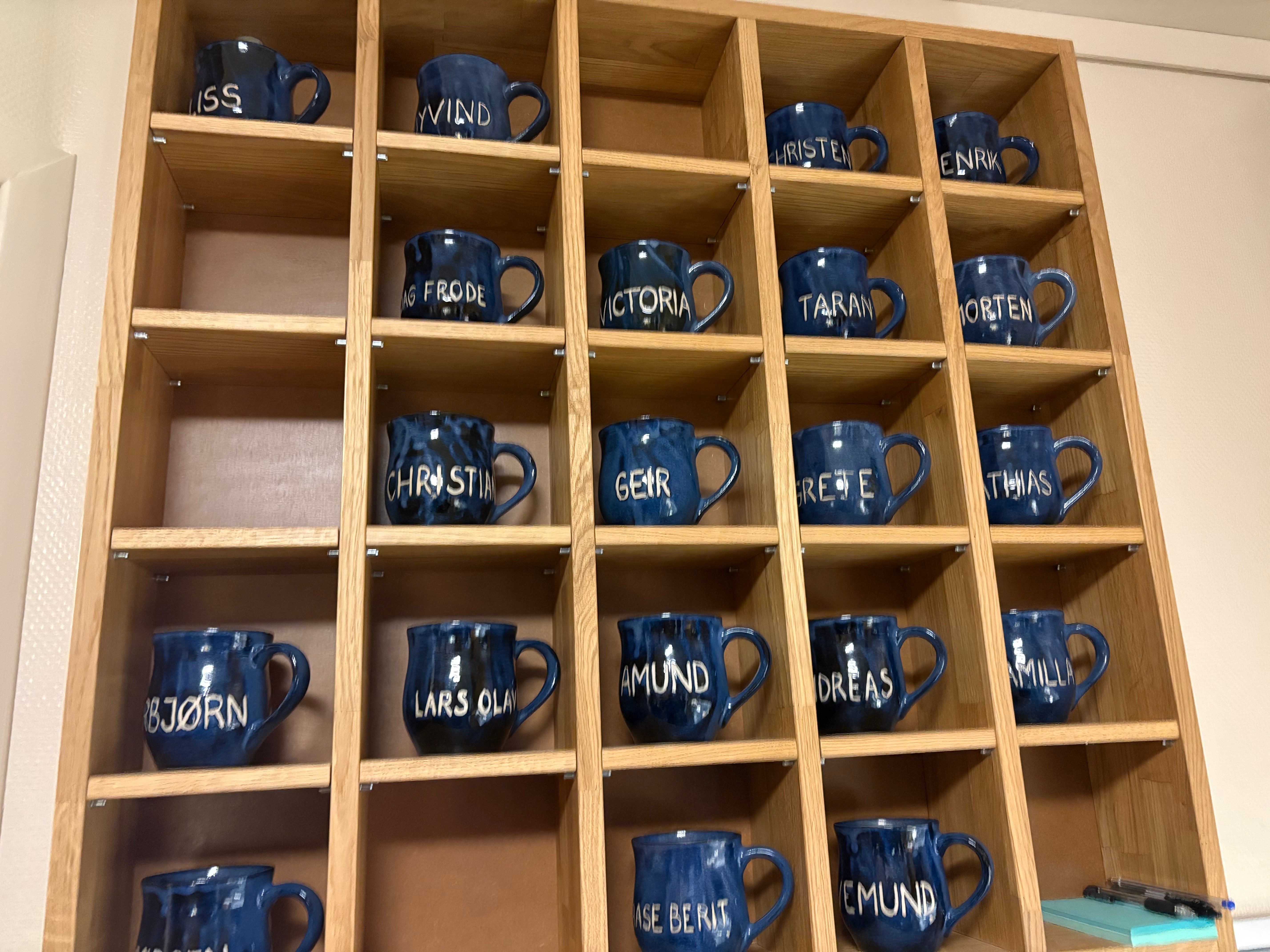 Hyller med blå kopper med navn på