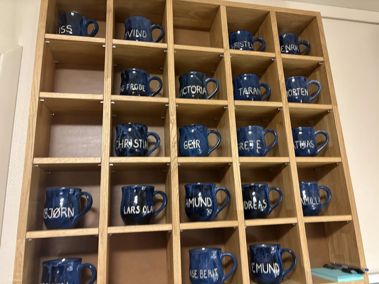 Hyller med blå kopper med navn på