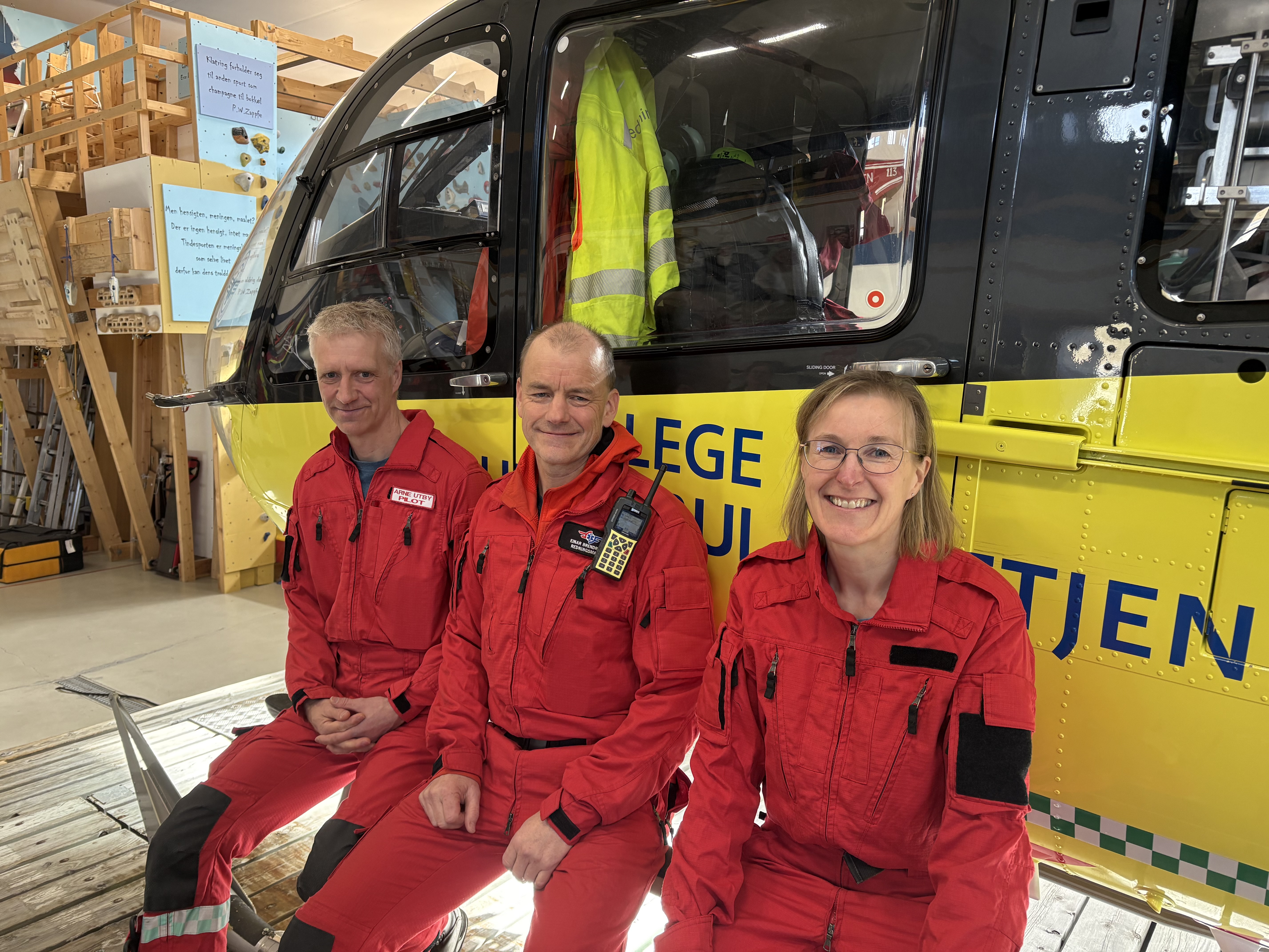 To menn og en kvinne i røde luftambulanseuniformer foran et helikopter