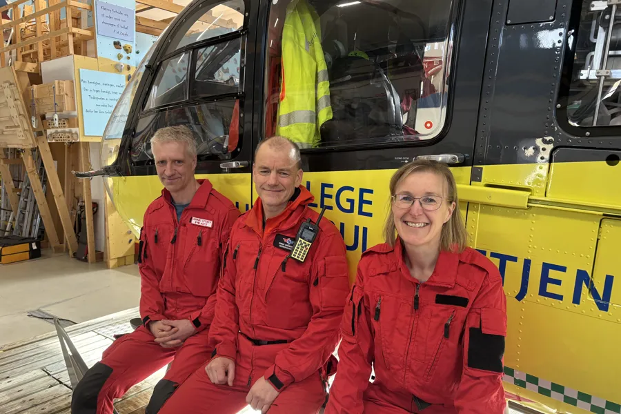 To menn og en kvinne i røde luftambulanseuniformer foran et helikopter