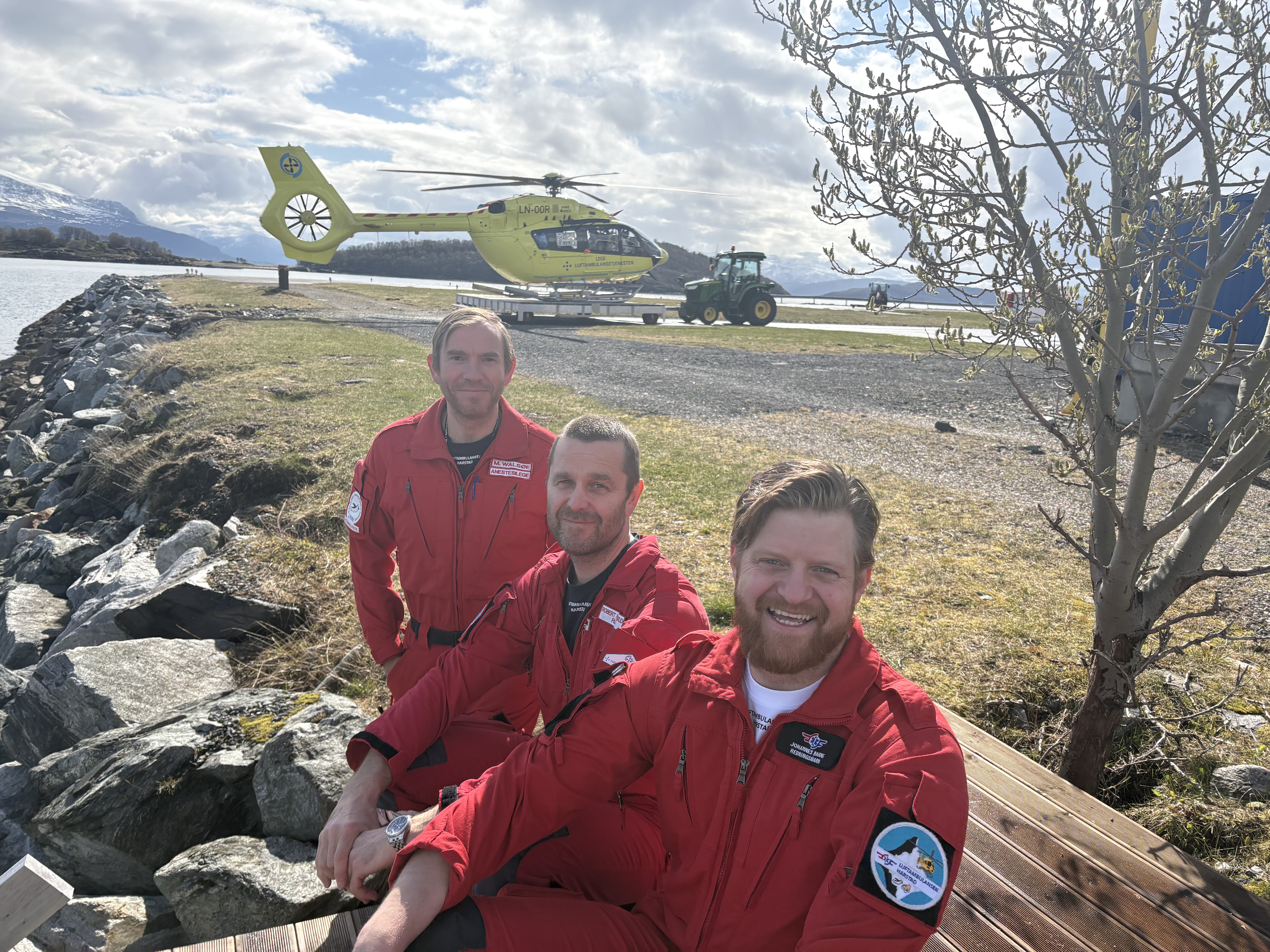 Tre menn i røde uniformer og et gult helikopter i bakgrunnen