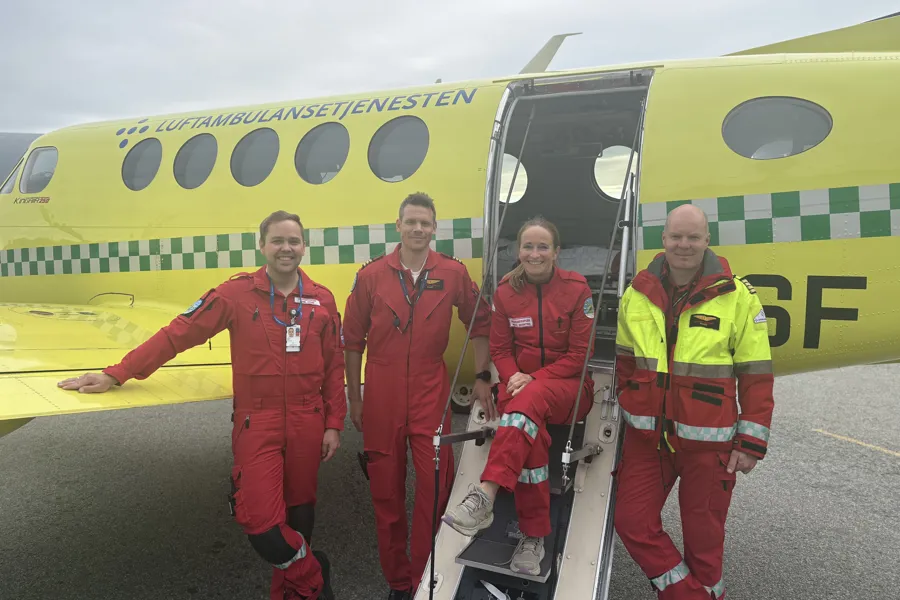 En gruppe menn i røde uniformer står foran et gult ambulansefly