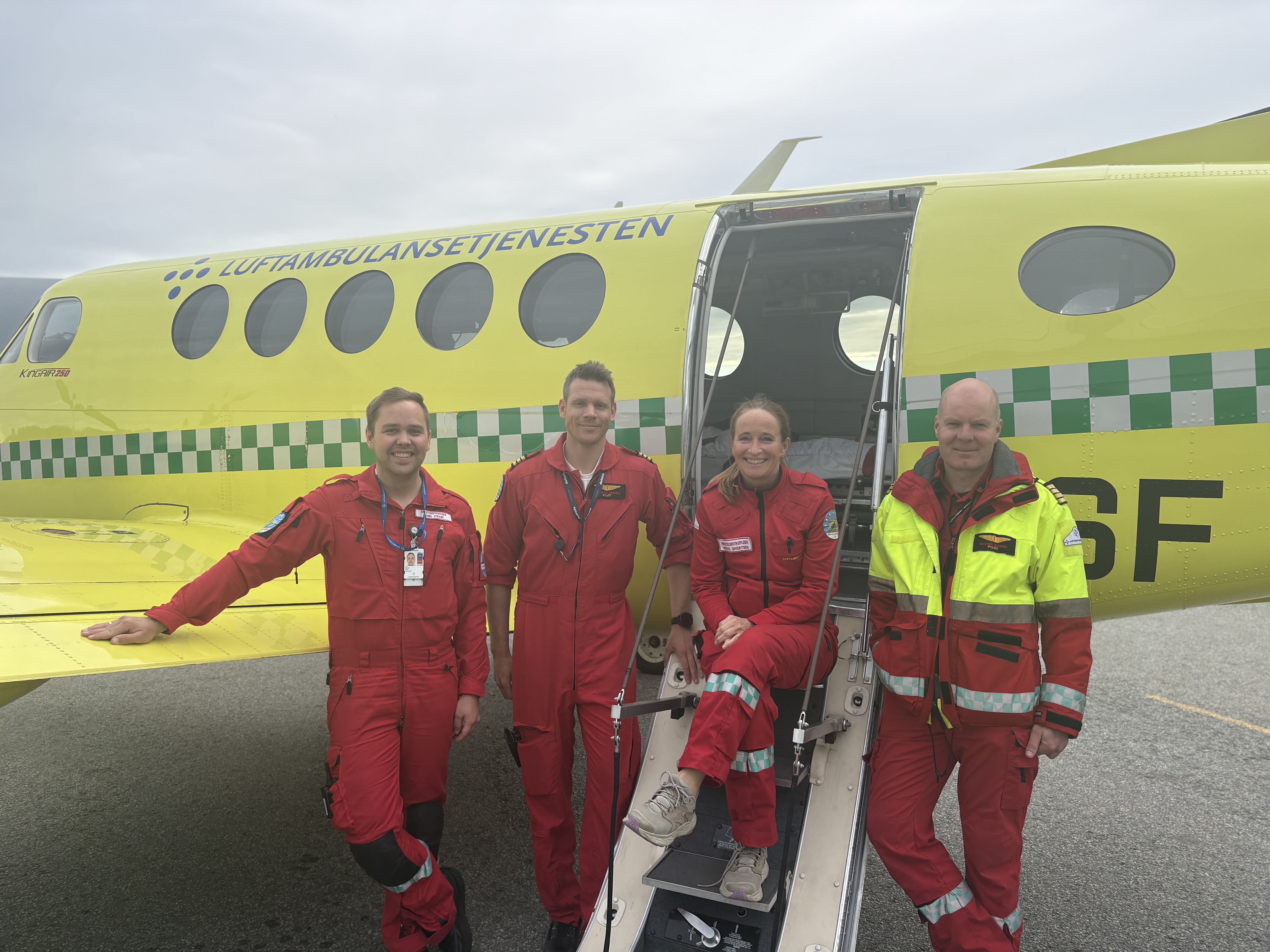 tre menn og ei dame  i røde kjeledresser står foran et ambulansefly