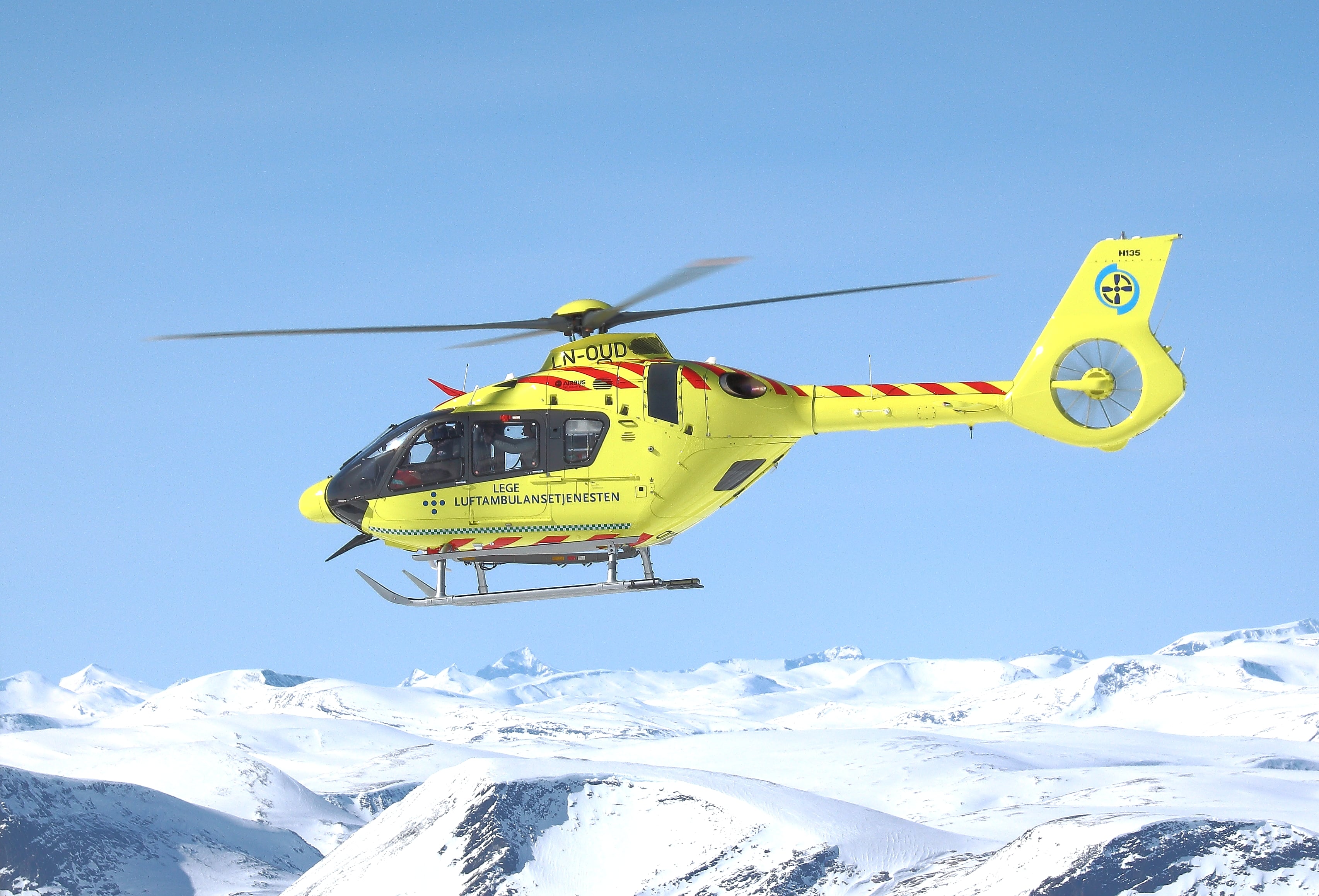 Et gult ambulansehelikopter over snødekte fjell