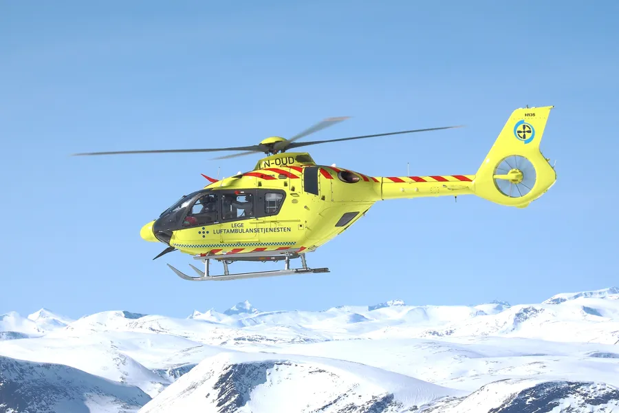 Et gult ambulansehelikopter over snødekte fjell