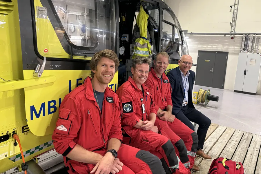 tre menn i uniform og en mann i dress sittende foran ambulansehelikopter