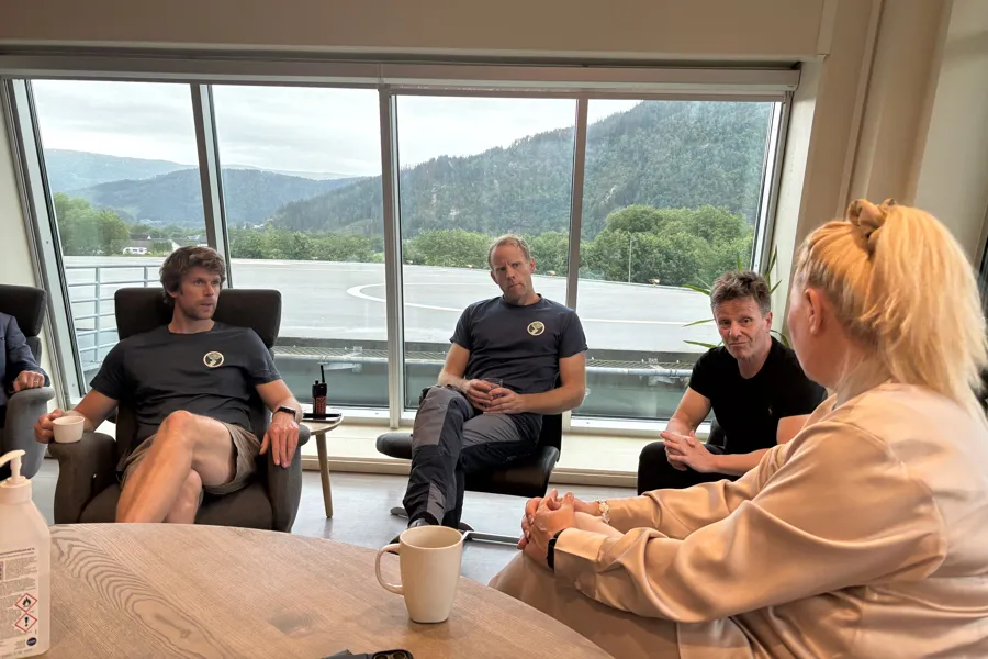 En kvinne sitter med ryggen til og snakker med tre menn