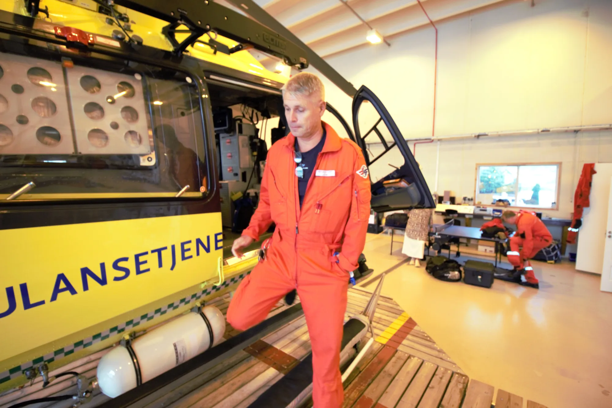En mann i rød jumpsuit som står ved siden av et helikopter