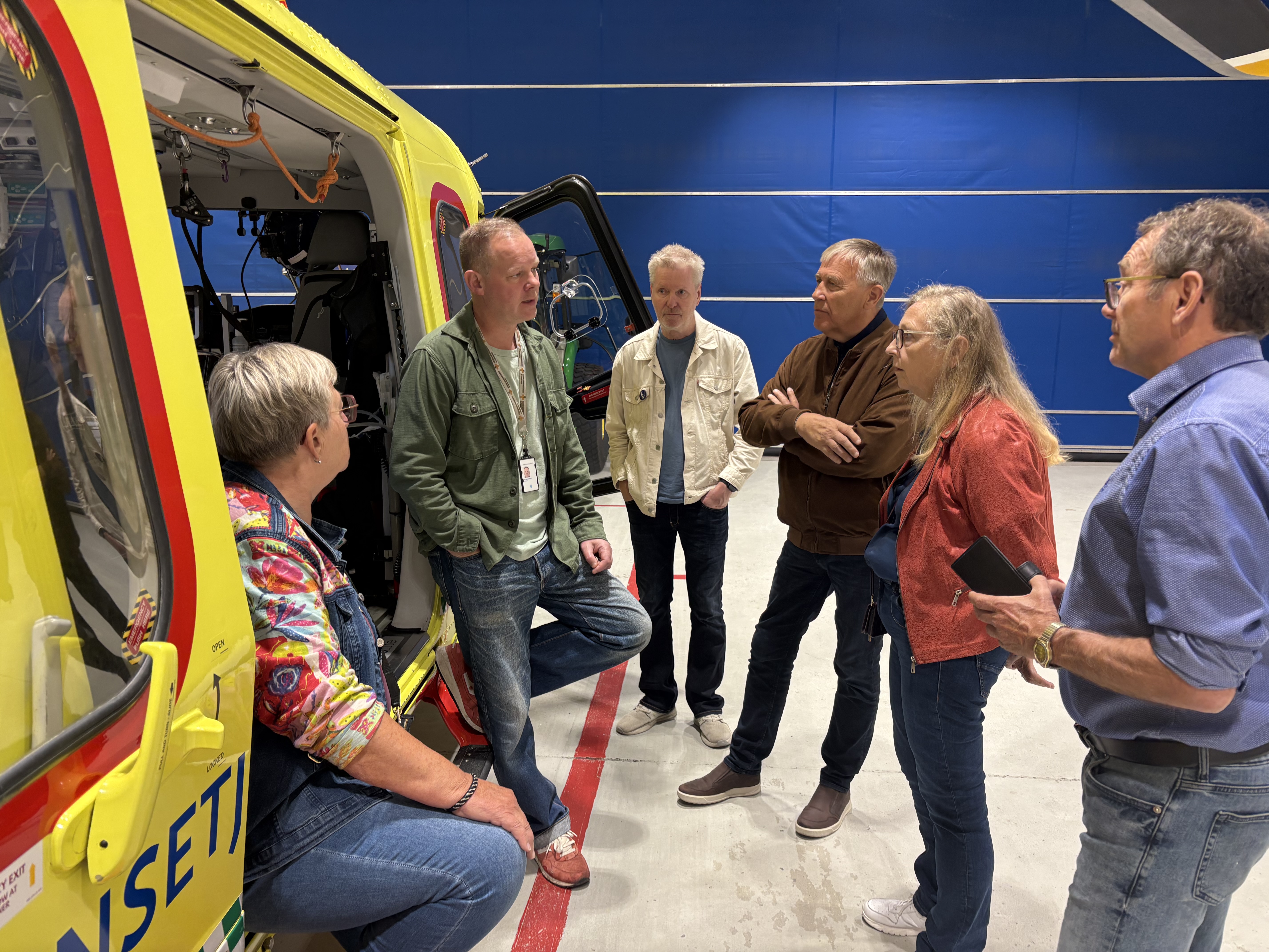 En snakker mann i åpningen på et ambulansehelikopter med tilhørere rundt