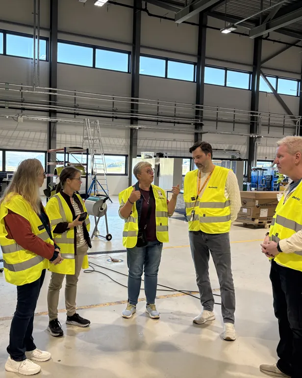 Tre damer og tre menn i refleksvest inne i en flyhangar