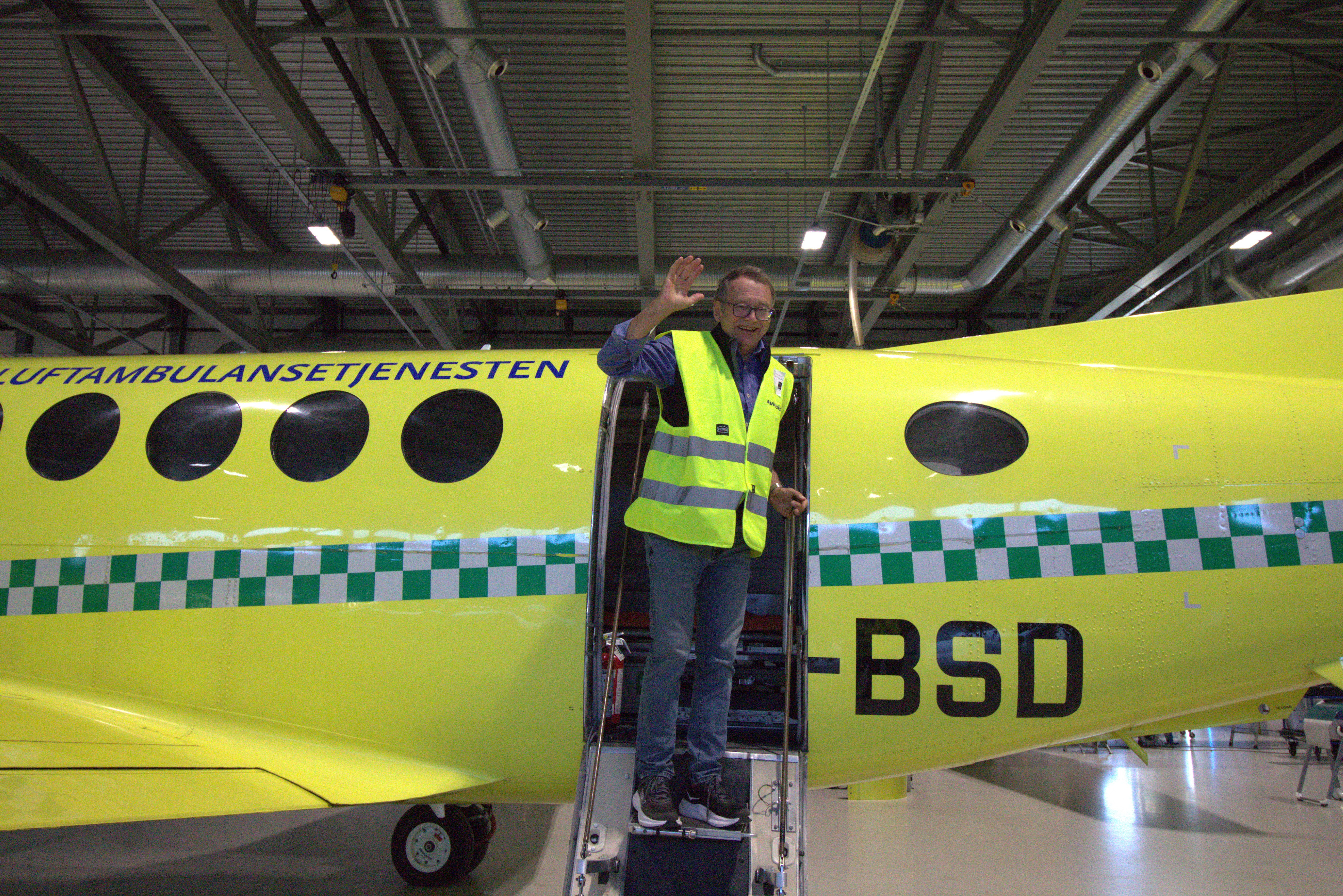 En mann i refleksvest vinker i flydøren på et ambulansefly