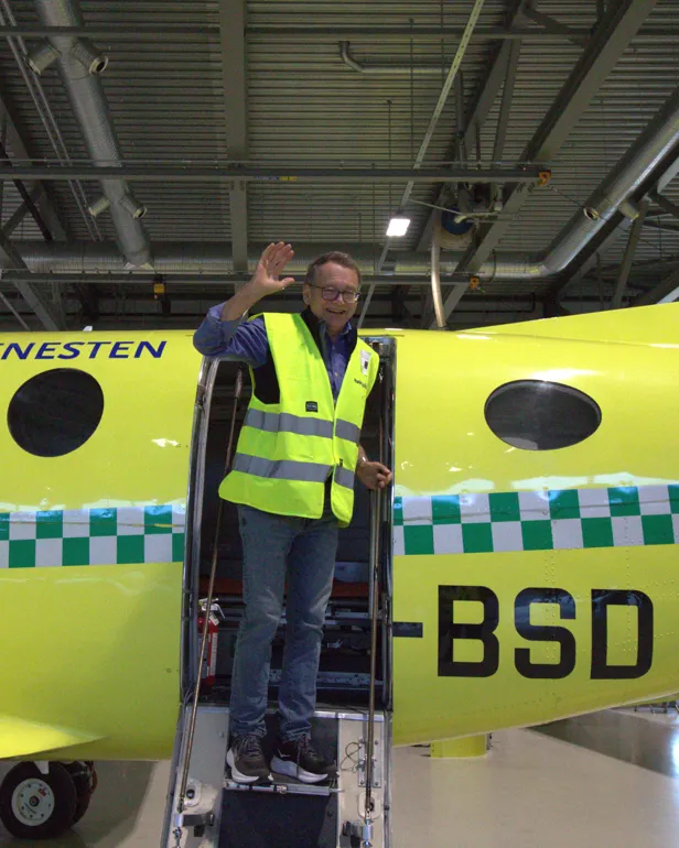 En mann i refleksvest vinker i flydøren på et ambulansefly