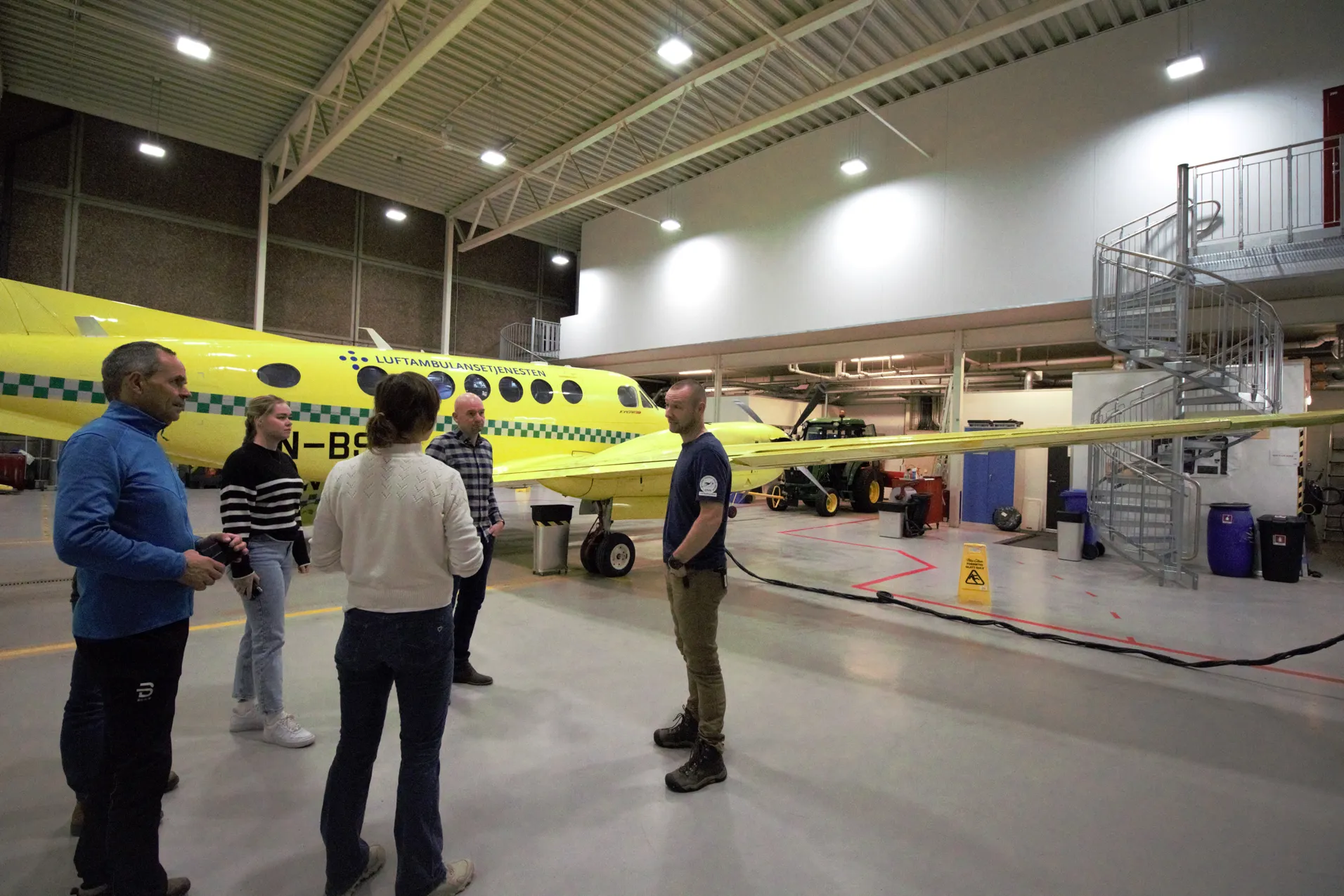 En gruppe mennesker står inne i en hangar foran et fly
