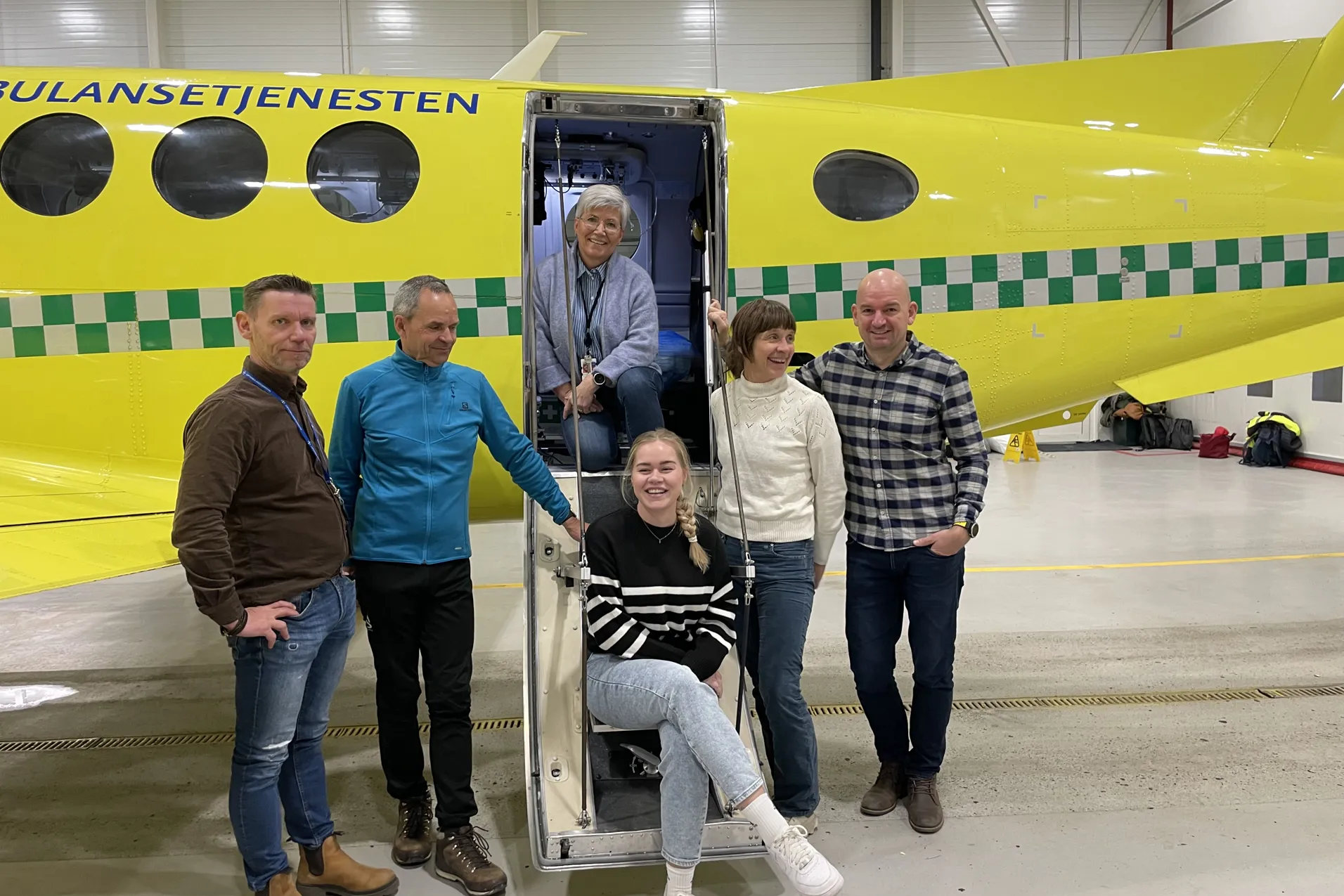 En gruppe mennesker som poserer for et bilde foran et gult ambulansefly