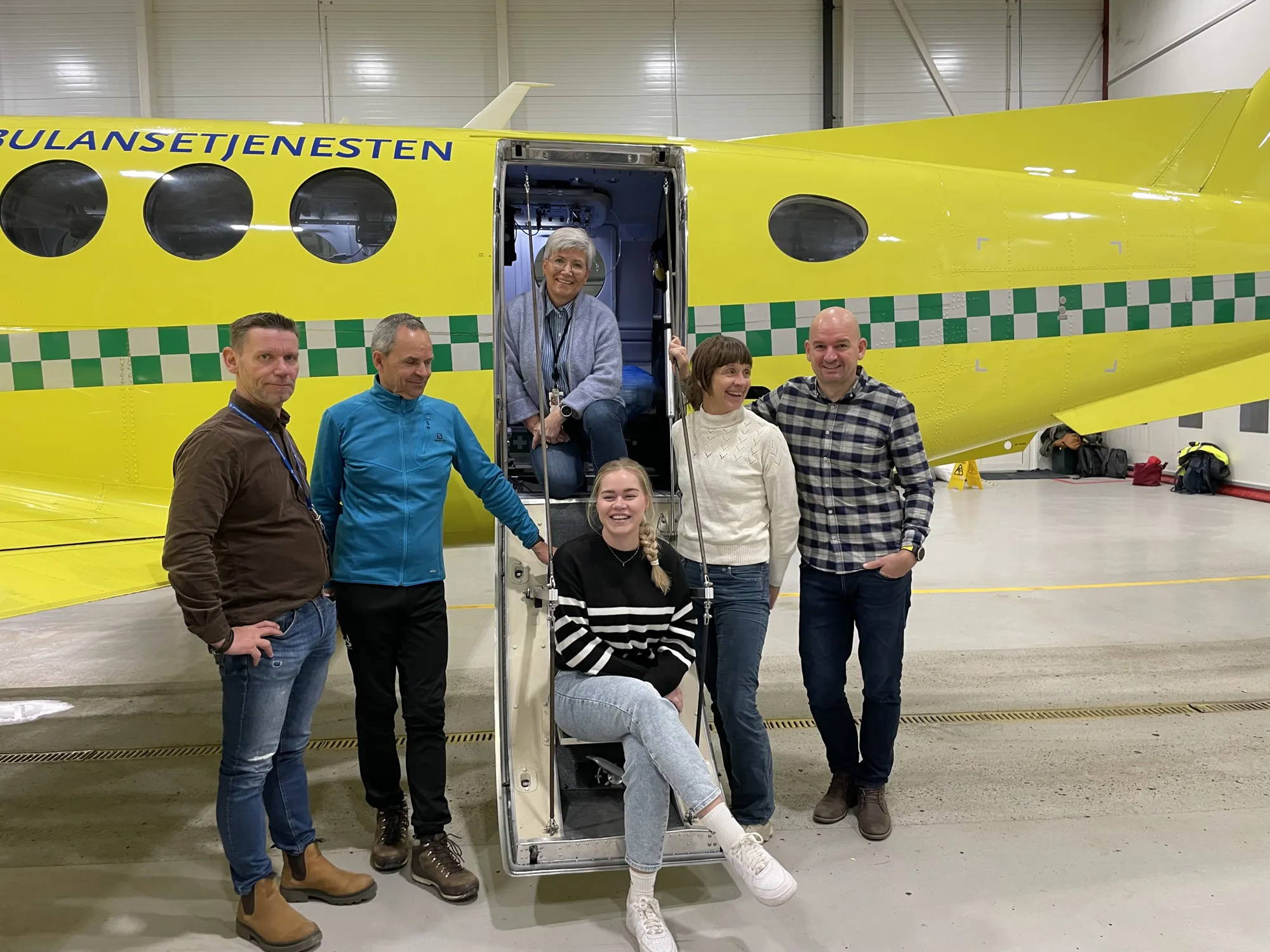 En gruppe mennesker som poserer for et bilde foran et gult ambulansefly