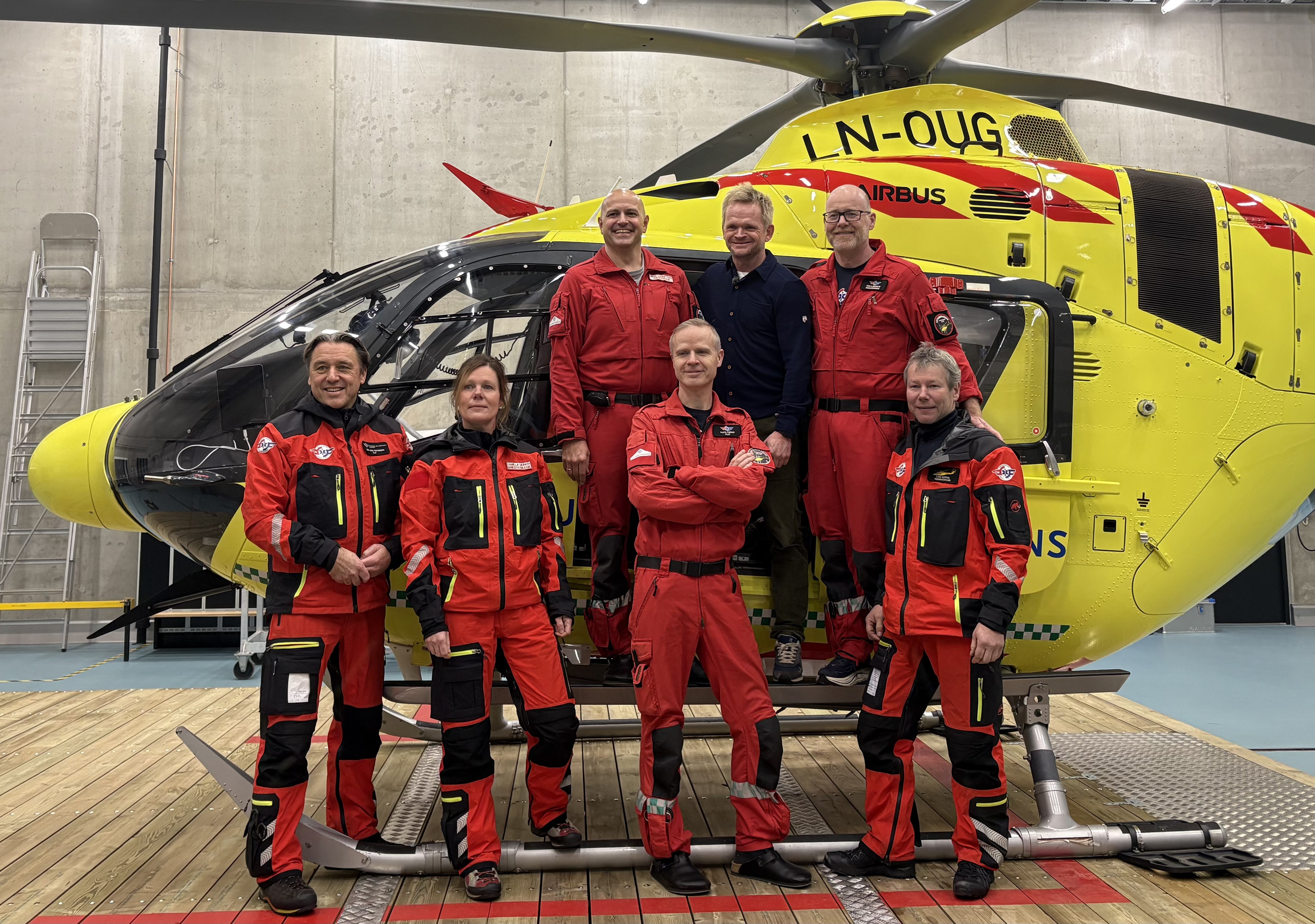 Helikoptercrew i røde dresser står foran et  gult helikopter