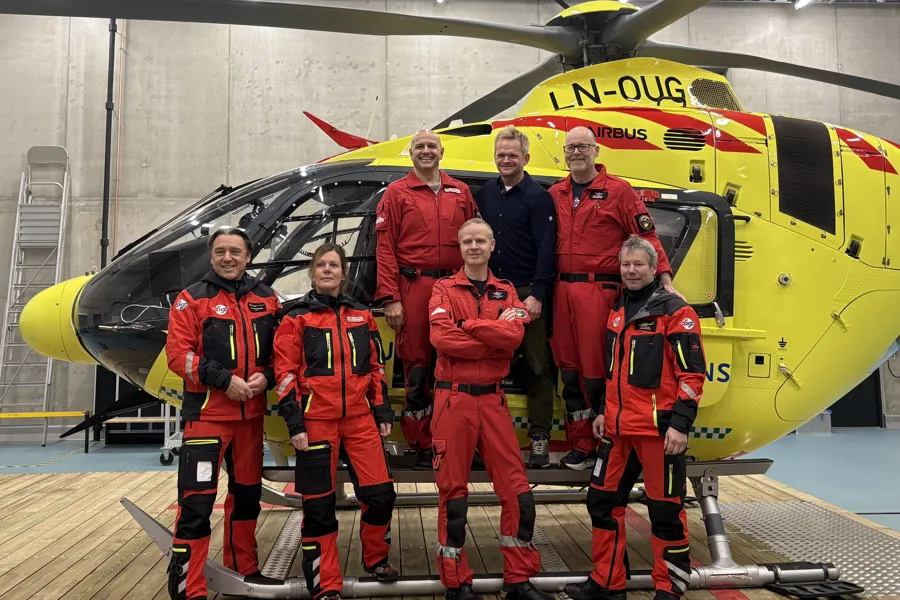 Helikoptercrew i røde dresser står foran et gult helikopter